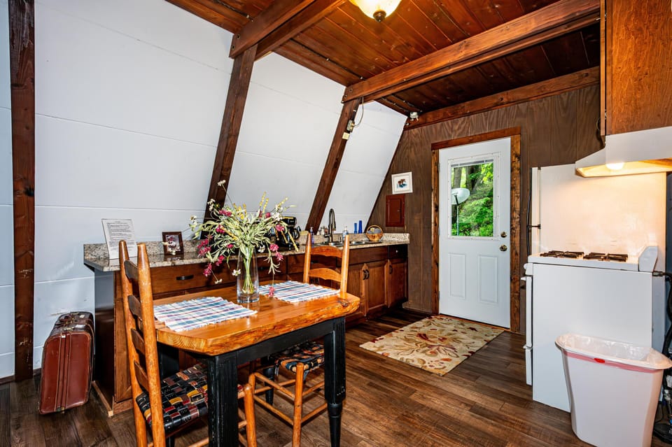 Dining area with rustic wood table, woven seat chairs, granite countertop, and white door overlooking greenery.