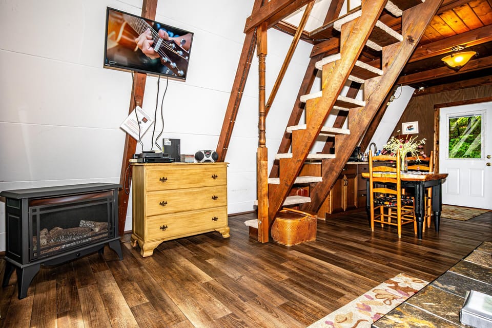 Wood-paneled staircase with carpeted steps beside a yellow dresser, electric fireplace, and dining area with wooden chairs.