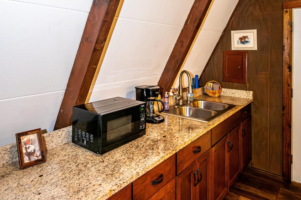 Granite countertop kitchen with double stainless steel sink, dark wood cabinets, and a black microwave.