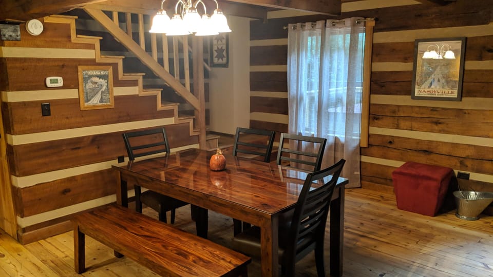 Polished wood dining table with black ladder-back chairs and bench under a multi-bulb chandelier.