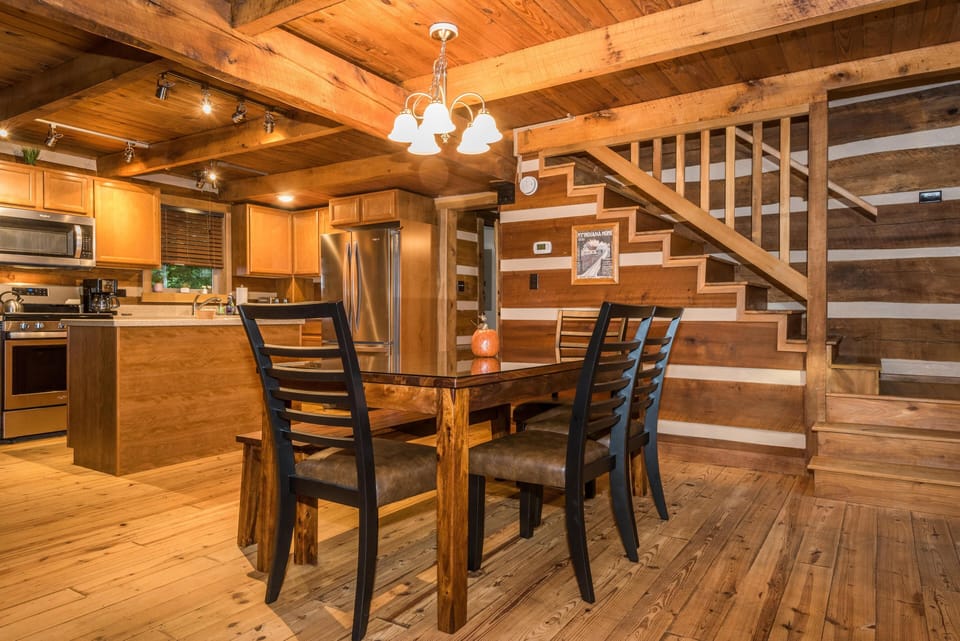 Dining area with a dark wood table, ladder-back chairs, and wood-paneled walls beside the staircase.