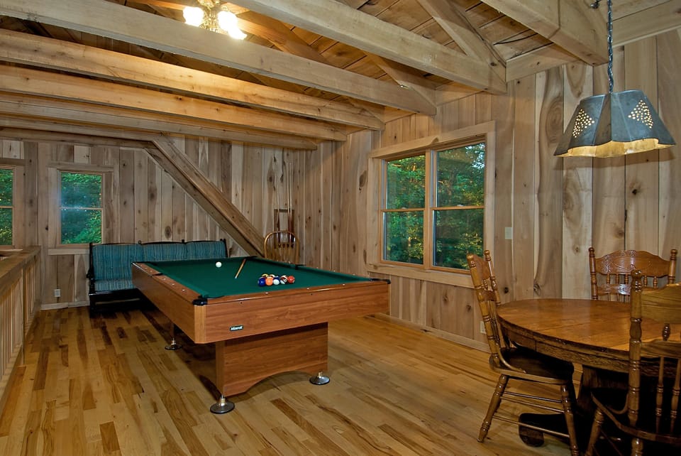 Game room featuring a wooden pool table, round dining table with carved chairs, and exposed ceiling beams.