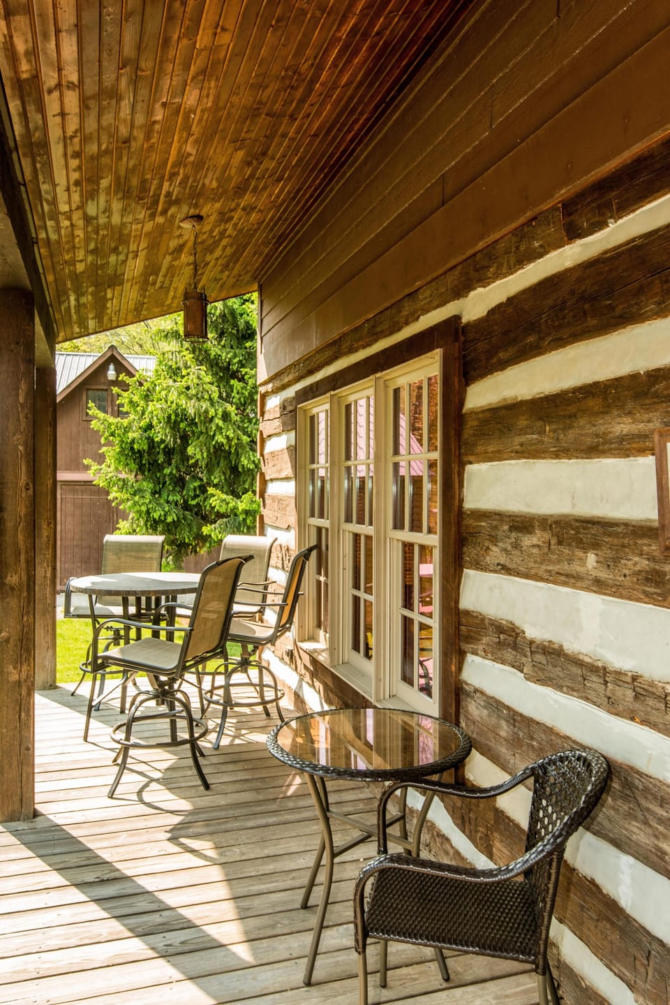 Covered porch with rustic log siding, wooden plank floor, glass-top table, and swivel patio chairs.