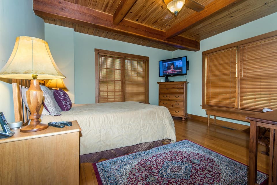 Bedroom featuring exposed wood beams, hardwood floors, patterned area rug, and a mounted flat-screen TV.