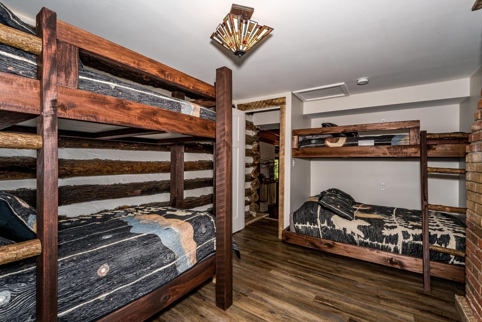 Bunk bedroom with two dark stained wood beds, black nature-themed quilts, wood-look flooring, and log cabin walls.