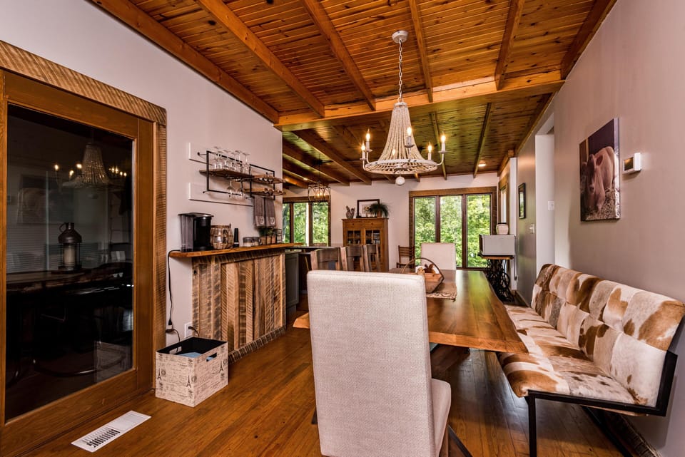 Dining area with a wooden table, upholstered chairs, a cowhide bench, and a beaded chandelier overhead.