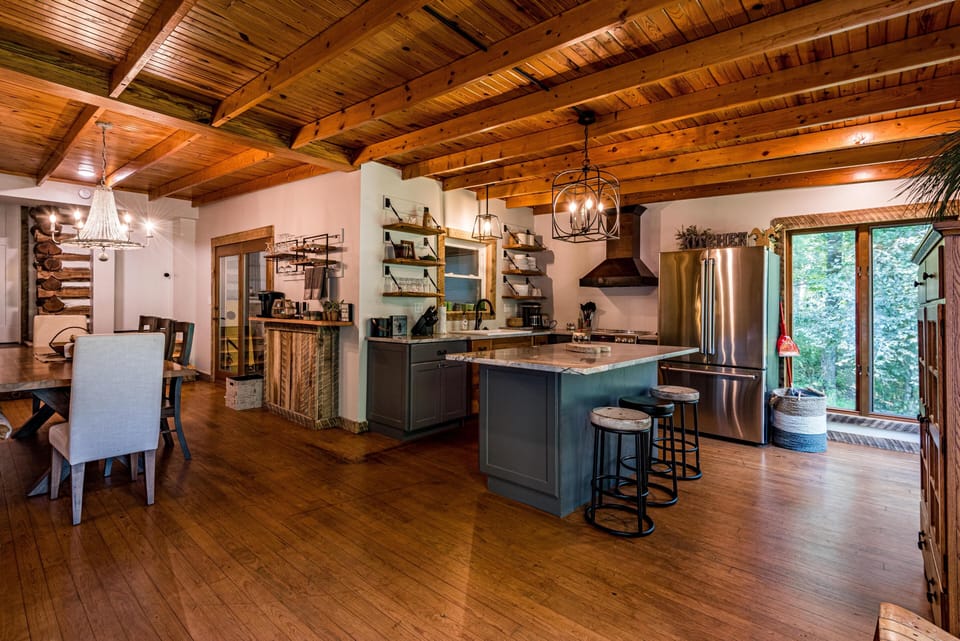 Open kitchen features gray cabinetry, marble island with three stools, and stainless steel appliances.