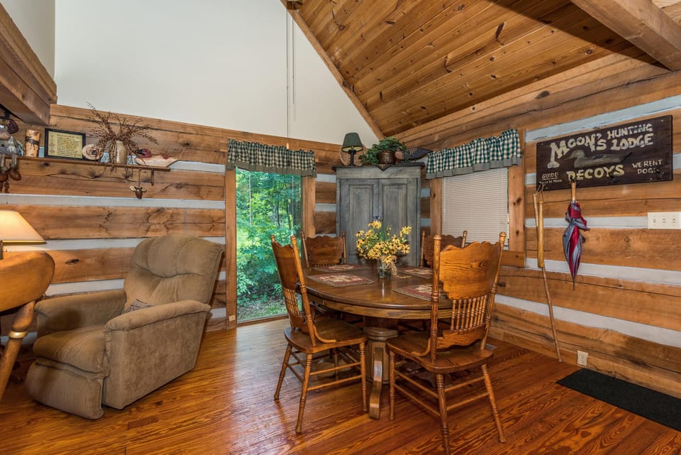 Natural light filters through plaid valances above a glass door, highlighting the hardwood floors and wood-paneled walls in the dining space.