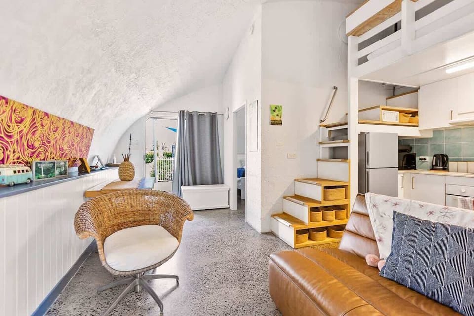 Unwind beneath the dome’s soaring curved ceiling in the relaxed living area, where comfortable seating, coastal artwork, air conditioning, and soft natural light create an easygoing tropical atmosphere.