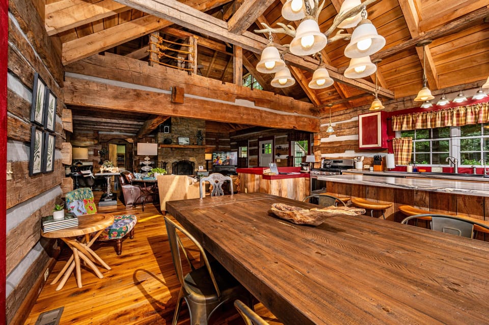 Wide plank wood floors and exposed beam ceiling surround the dining table and open kitchen with red accents.