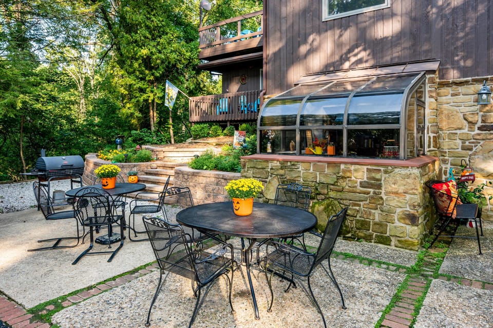 Metal mesh patio tables and chairs sit on a stone and brick terrace beside a stone planter with glass enclosure.