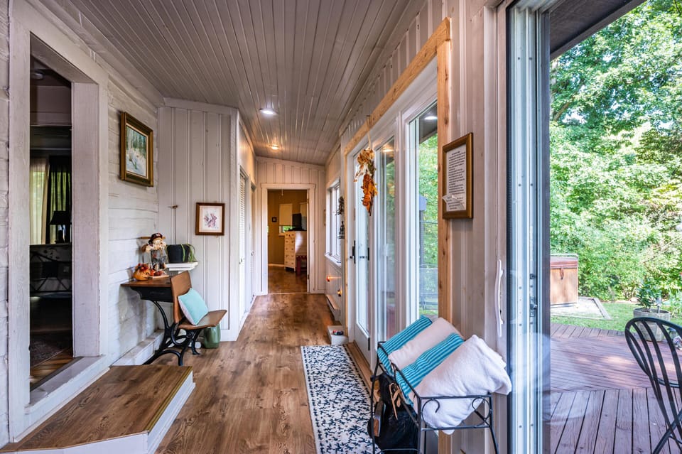 Sunroom with wood-look flooring, white beadboard walls and ceiling, a vintage school desk, and glass doors to the deck.