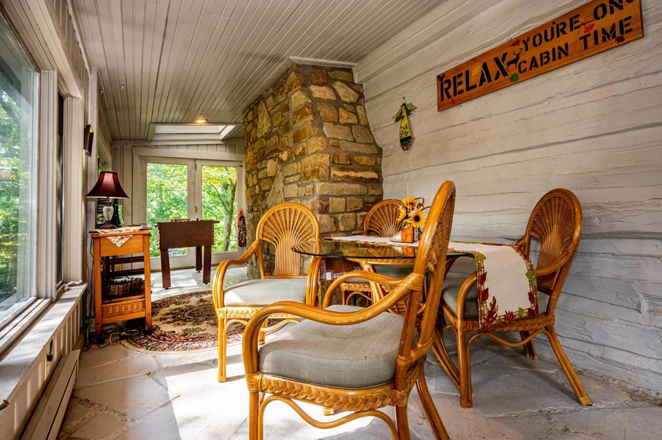 Natural light fills the sunroom with stone flooring, painted log walls, a foosball table, and a stone chimney centerpiece.
