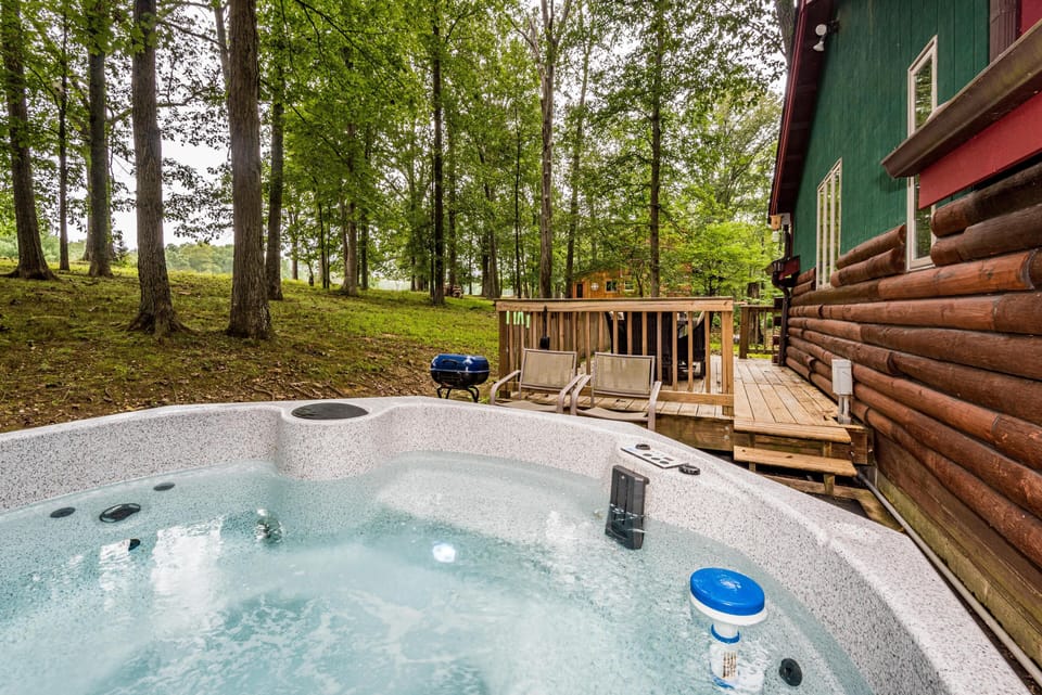 Hot tub with bubbling water beside green cabin exterior and wooden deck.