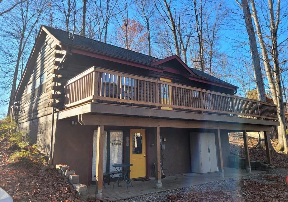 Exterior view showing natural wood siding, yellow front door, and wraparound upper deck railing.