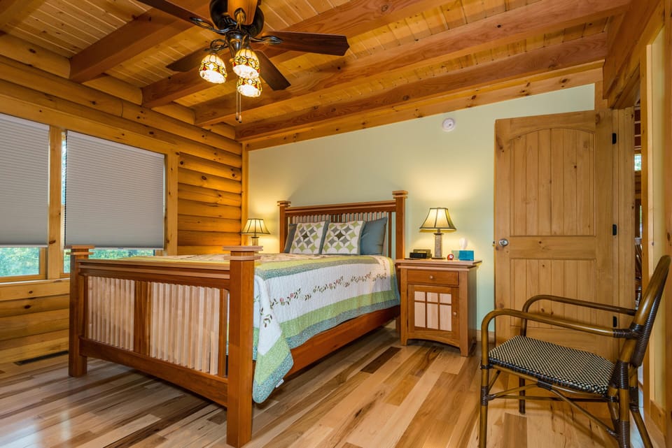 Master bedroom with wooden bed frame, patchwork quilt, matching nightstands, rattan chair, and ceiling fan.