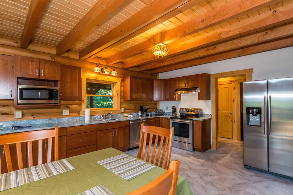 Kitchen with cherry wood cabinets, granite countertops, stainless steel appliances, and exposed wood beam ceiling.