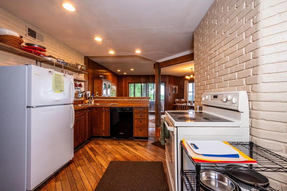 Hardwood floors lead past a white stove and refrigerator to wood cabinetry and a black dishwasher in the kitchen.