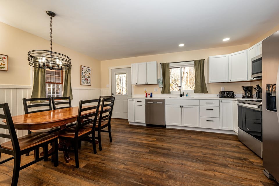 Open kitchen and dining area with white cabinetry, stainless steel appliances, wood dining table, and dark hardwood floors.