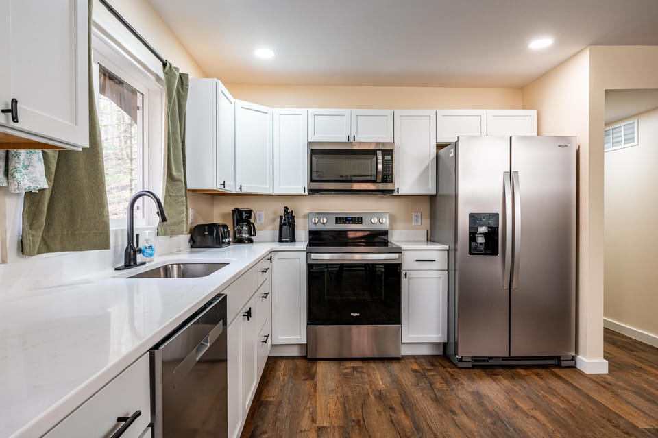 White cabinetry and quartz countertops surround stainless steel appliances in the kitchen with wood-tone flooring.