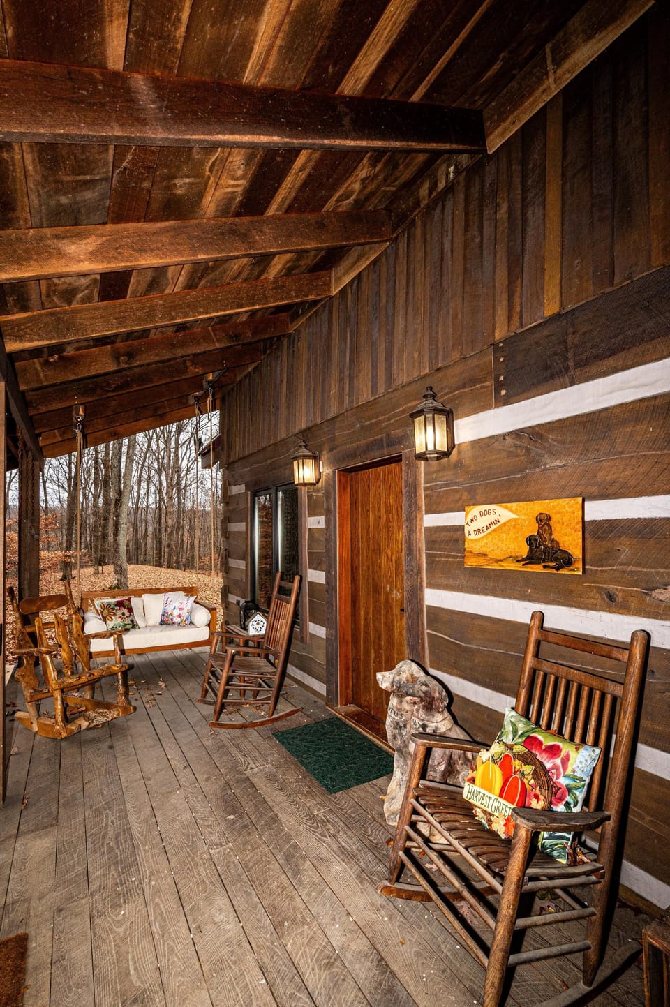 Large rustic porch with rocking chairs and warm wood accents, perfect for relaxing in a peaceful wooded setting.