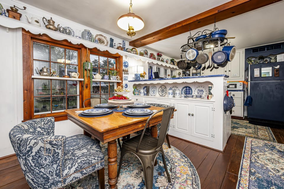 Wood dining table set with blue-and-white plates, surrounded by patterned and metal chairs beside large windows.