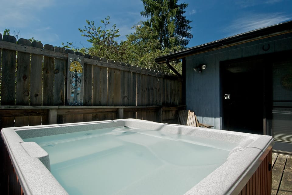 Water-filled hot tub with textured white edge sits on wooden deck beside blue exterior wall and fence.
