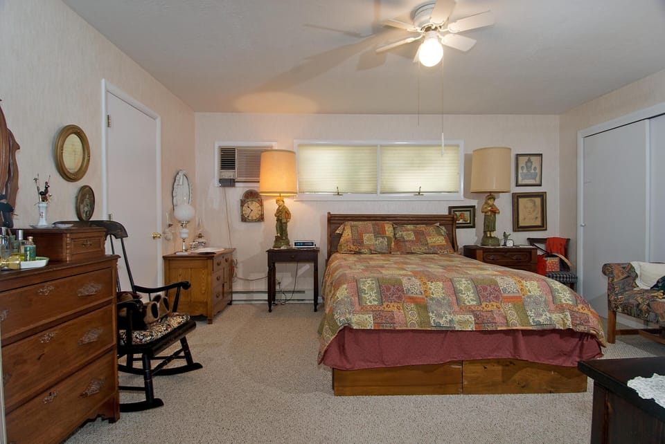 Bedroom features a wooden bed with patchwork quilt, two lamps on nightstands, and vintage framed artwork.