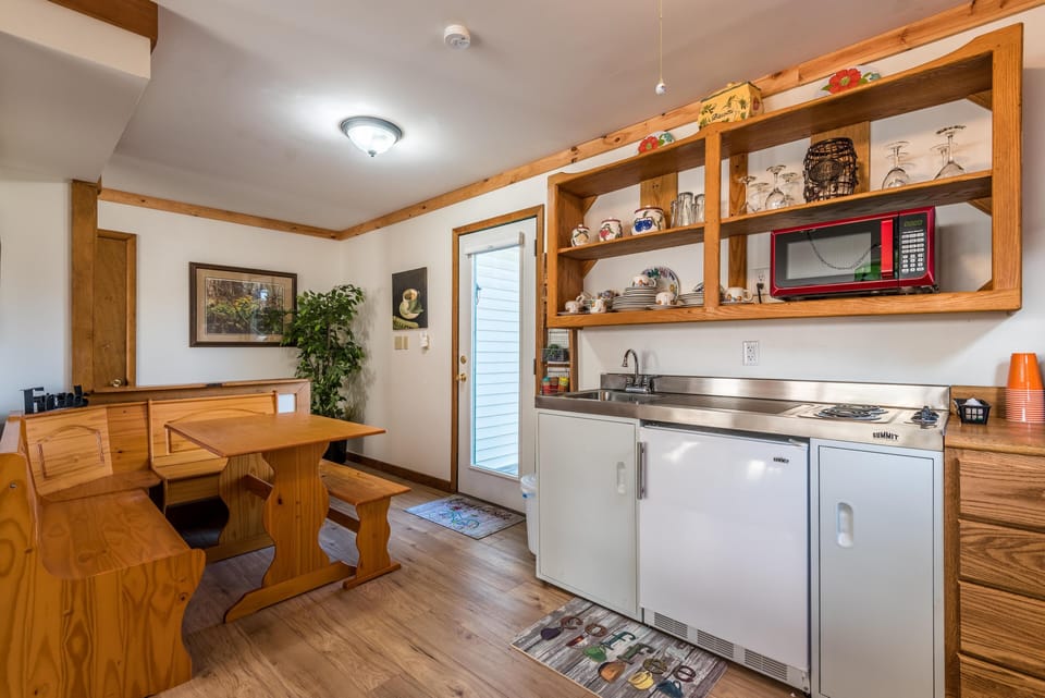Kitchen nook with built-in pine bench seating, open wooden shelves, and stainless steel sink and cooktop.