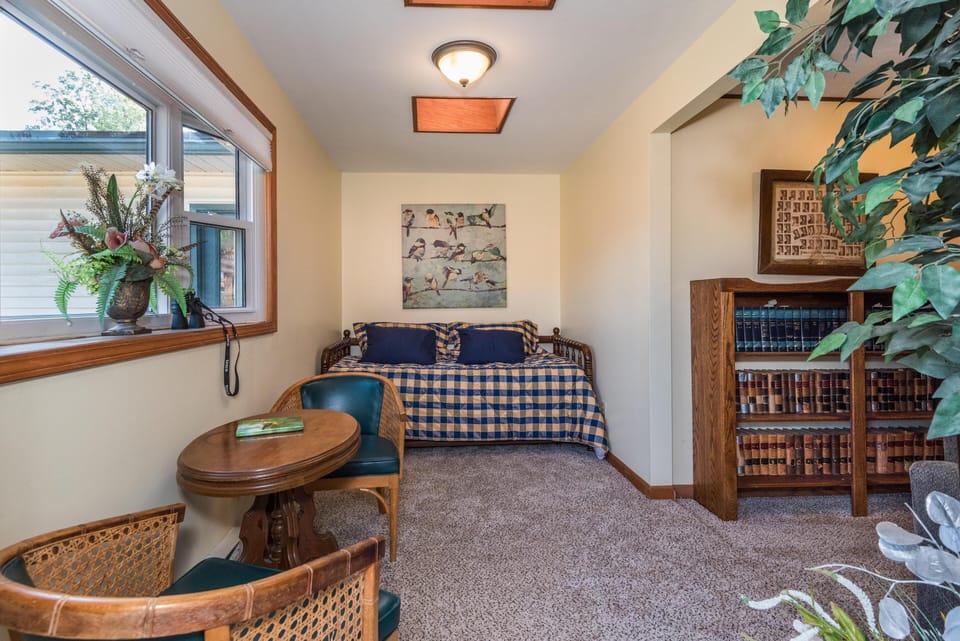 Small sitting area with round wooden table, cane-back chairs, and a daybed covered in blue plaid bedding.