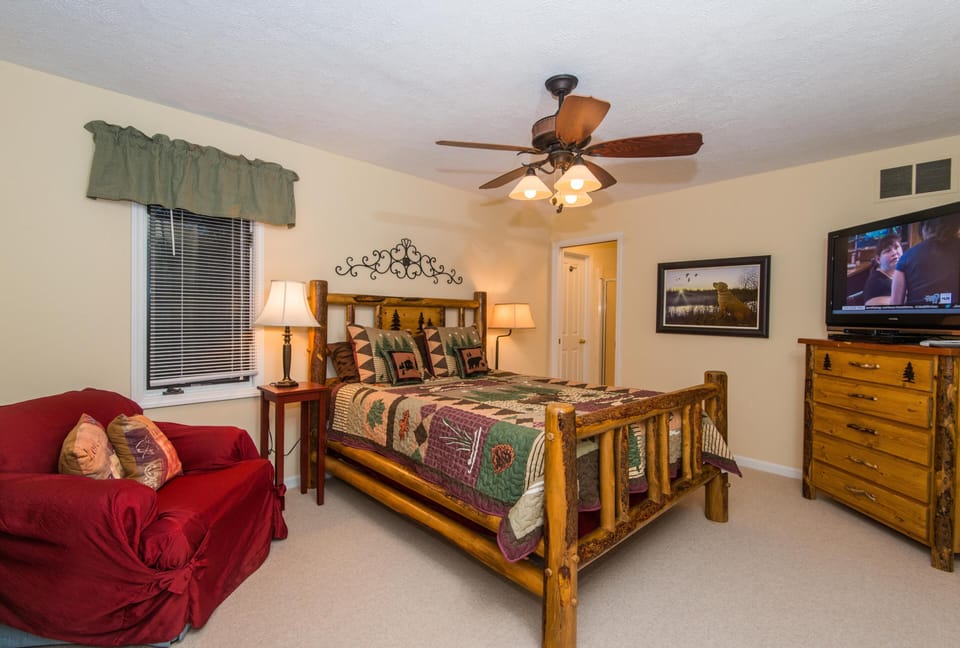 Bedroom with log frame bed dressed in forest-themed patchwork quilt and red slipcovered armchair.
