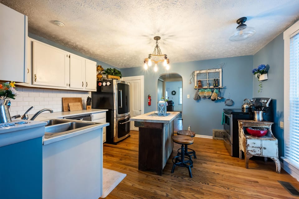 Blue walls and white cabinets surround a farmhouse island with wood stools and vintage decor in the kitchen.