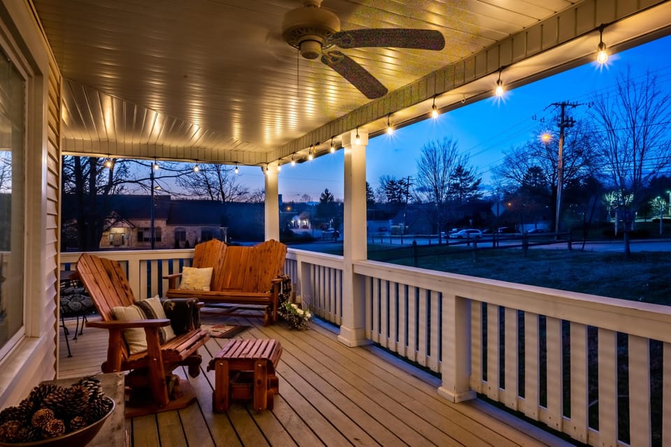 Evening glow highlights the covered porch with wood Adirondack chairs, string lights, and a ceiling fan.