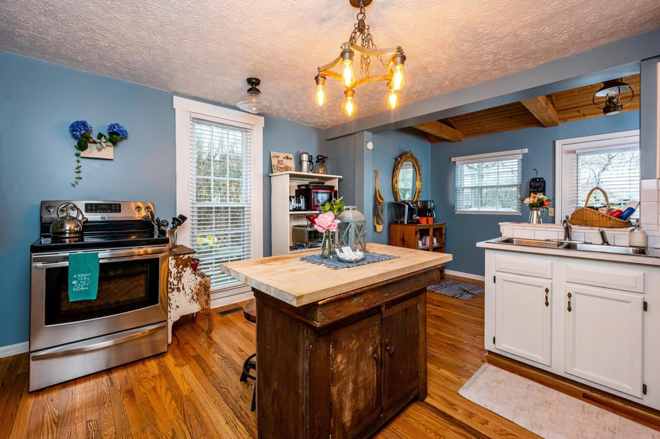 Rustic kitchen island with butcher block countertop sits on hardwood floors beneath Edison bulb chandelier.