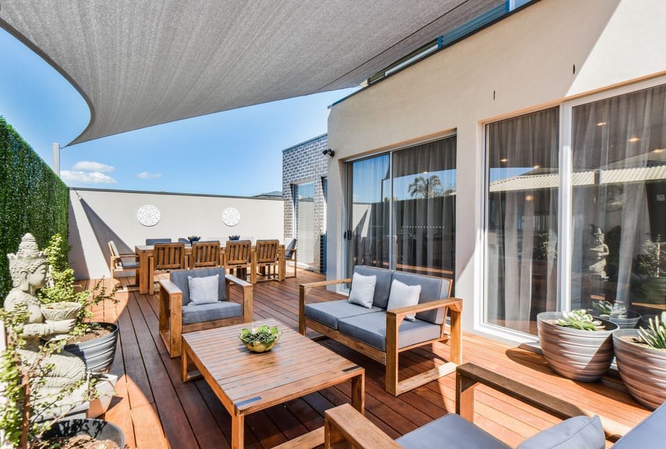 Outdoor deck area with large dining table, outdoor lounges, party lights and a gas heater