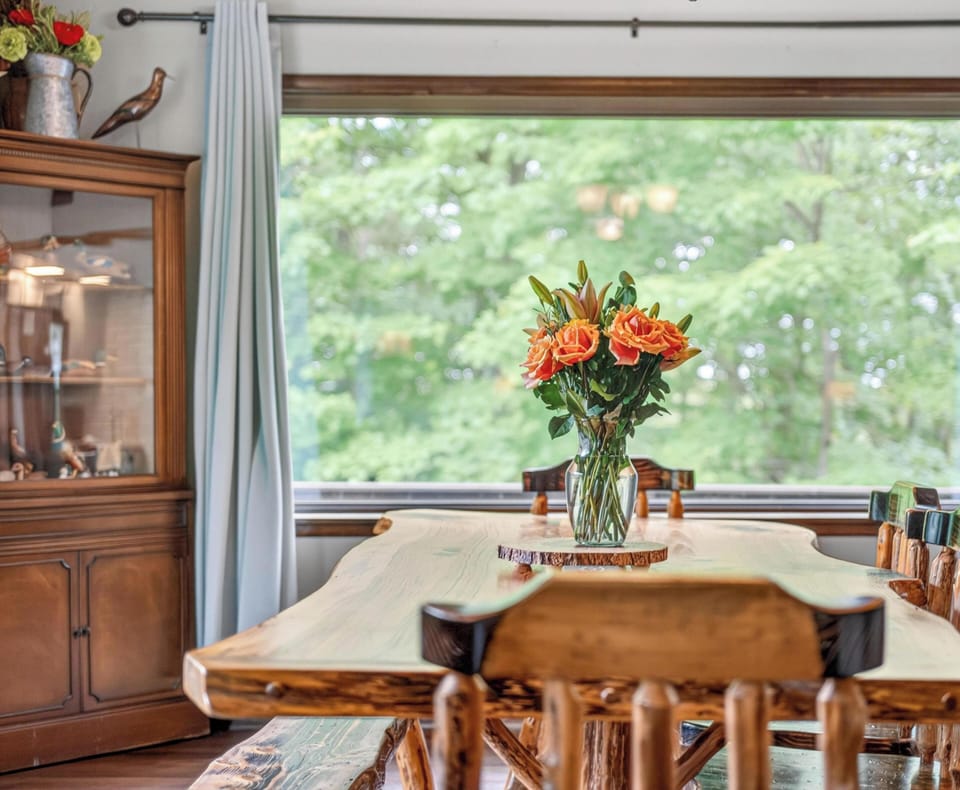 Rustic wood dining table and chairs centered beneath a large window framed with pale blue curtains.
