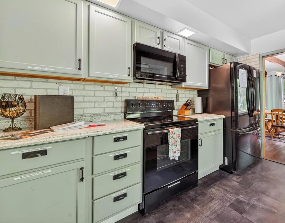 Muted green cabinets line the kitchen wall with black appliances and a marble-patterned countertop.