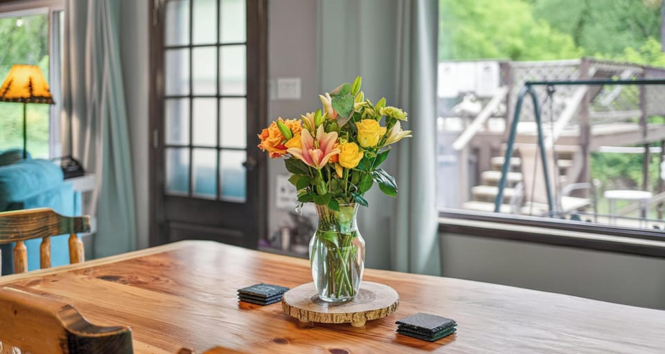 Rustic wood dining table topped with a glass vase of fresh flowers, positioned by a window and door.