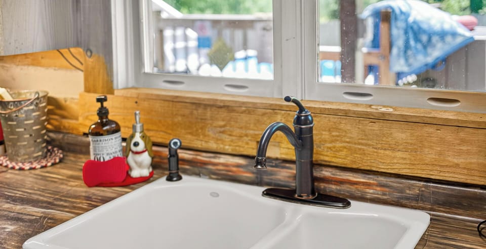 White double basin sink set into woodgrain countertop beneath a wide window with a wooden sill.