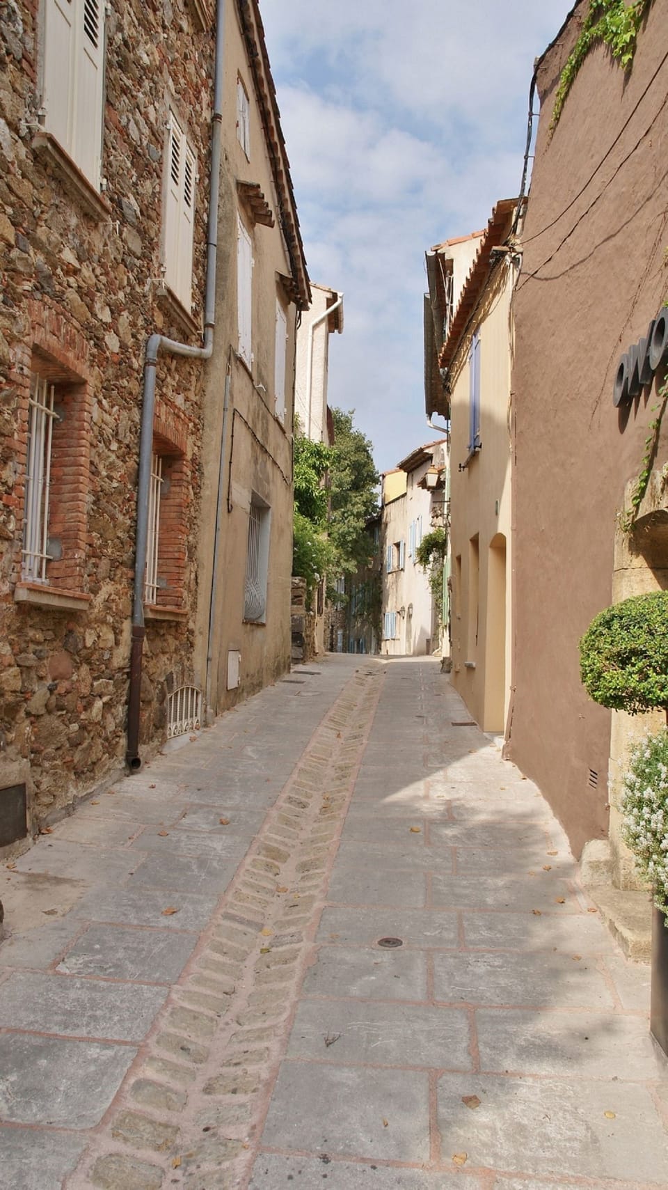 A quiet sun-bleached lane winds between rustic stone and render facades in the heart of Grimaud's picturesque medieval village.