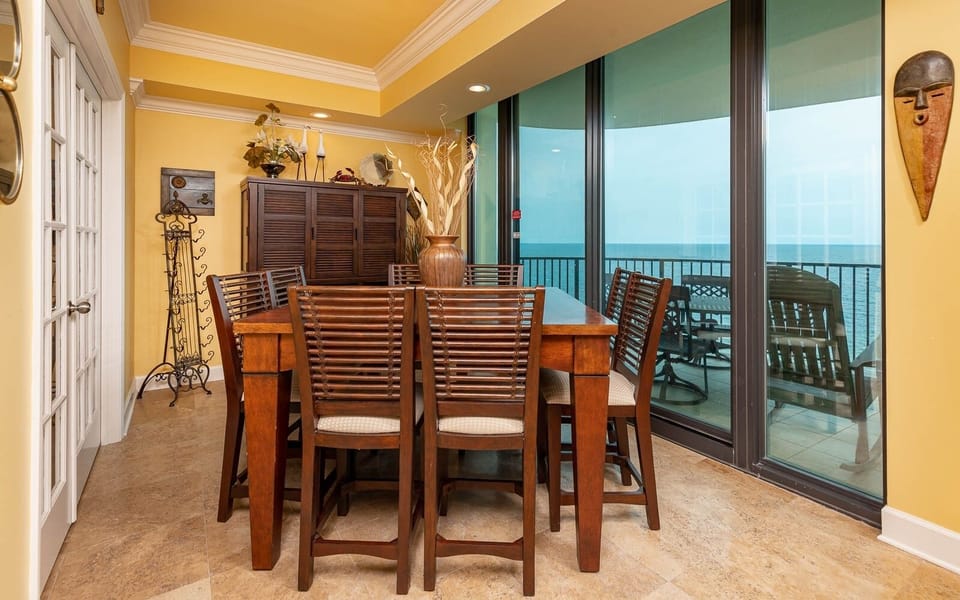 Dine at the spacious wooden table with comfortable seating, enjoying the coastal views through large glass doors
