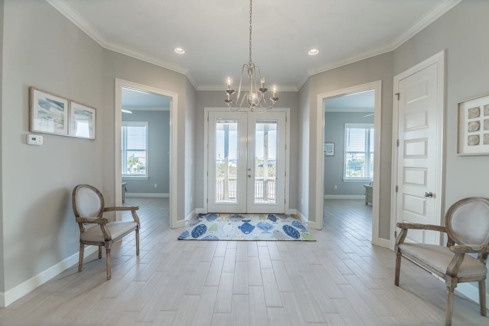Bright, open foyer with elegant chandelier and beach-inspired accents. French doors and large windows fill the space with light, creating a welcoming entrance to your Dauphin Island vacation home.