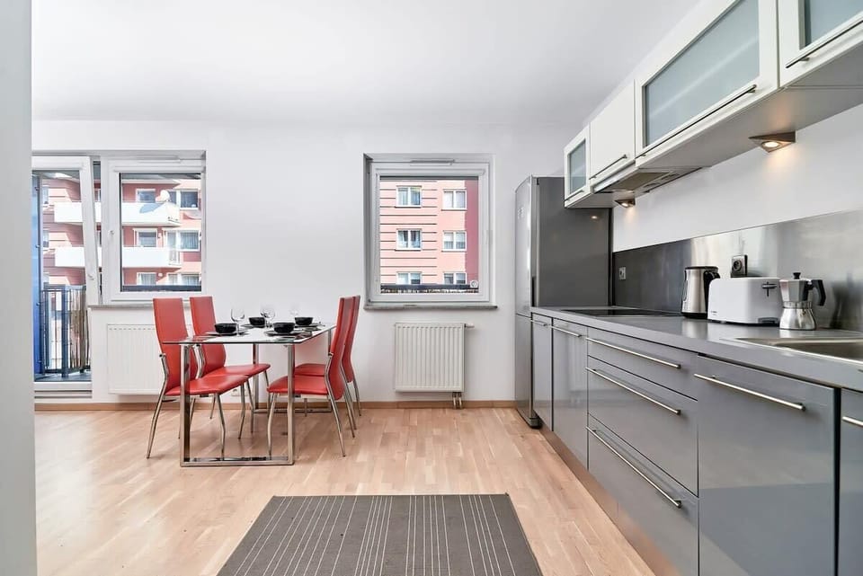 A spacious kitchen with sleek, gray cabinets and a window providing natural light. There's a refrigerator, oven, and plenty of counter space.