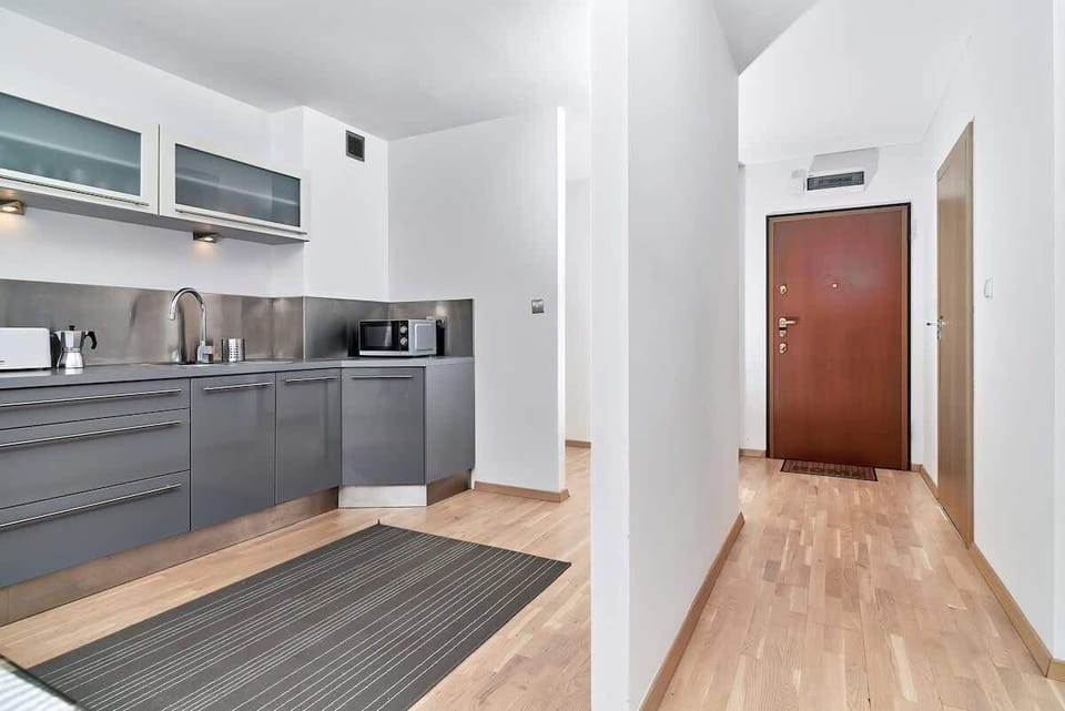 A modern kitchen with gray cabinets, built-in appliances, and light wooden flooring. A large fridge stands next to ample counter space.