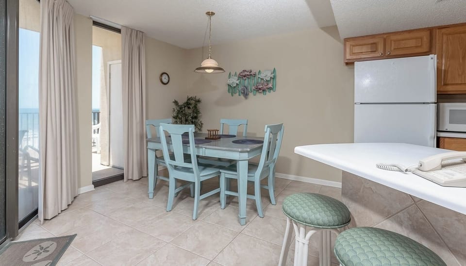 Bright dining area features a light blue table set for four, with a view of the beach through large sliding glass doors