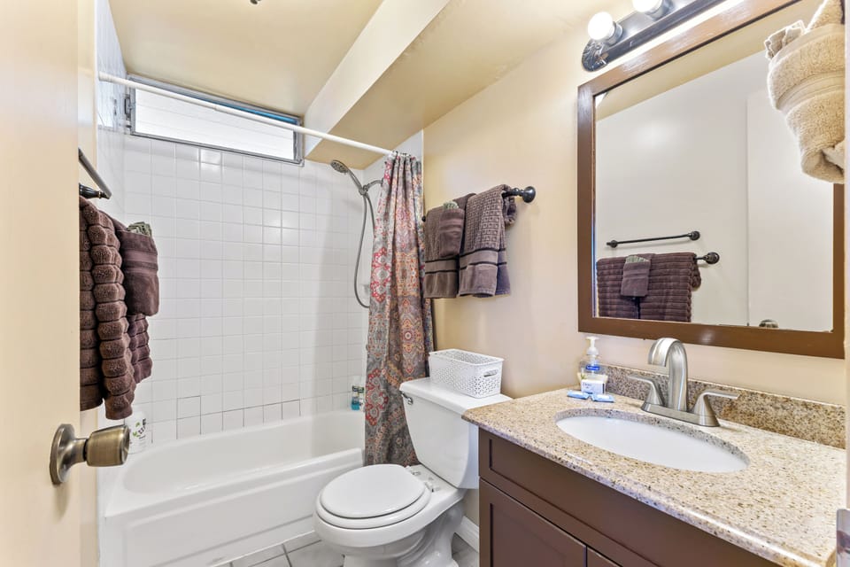 Bath tub and shower with linens, shampoo, conditioner, soap, hair dryer.
