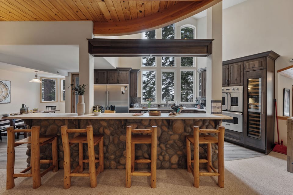 Spacious kitchen with a stone-front breakfast bar, vaulted ceilings, and forest-facing windows.