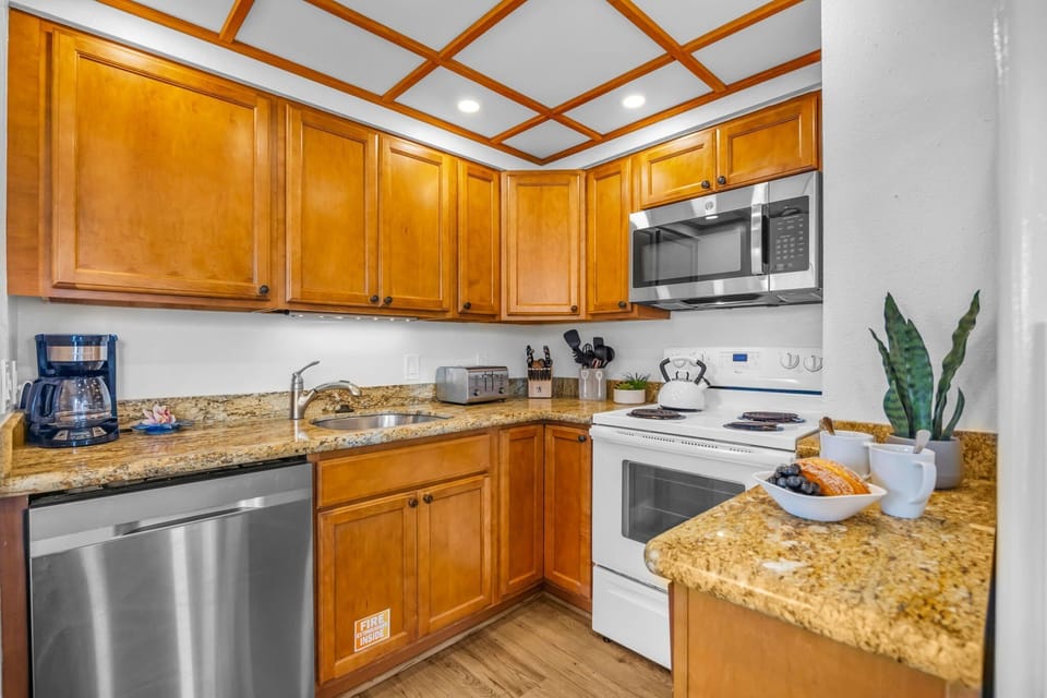 Modern kitchen with wood cabinetry, granite counters, and stainless appliances under a decorative ceiling grid.