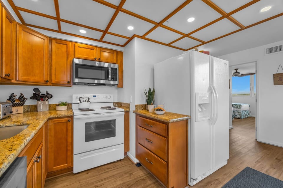Wooden cabinetry, white appliances, and a grid‑pattern ceiling give the kitchen a clean, functional look.