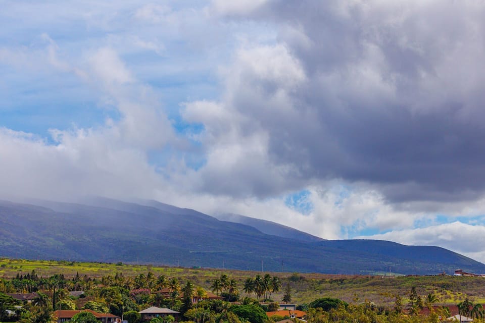 Lush green landscape stretches toward the mountains, with scattered homes nestled under a cloudy sky.